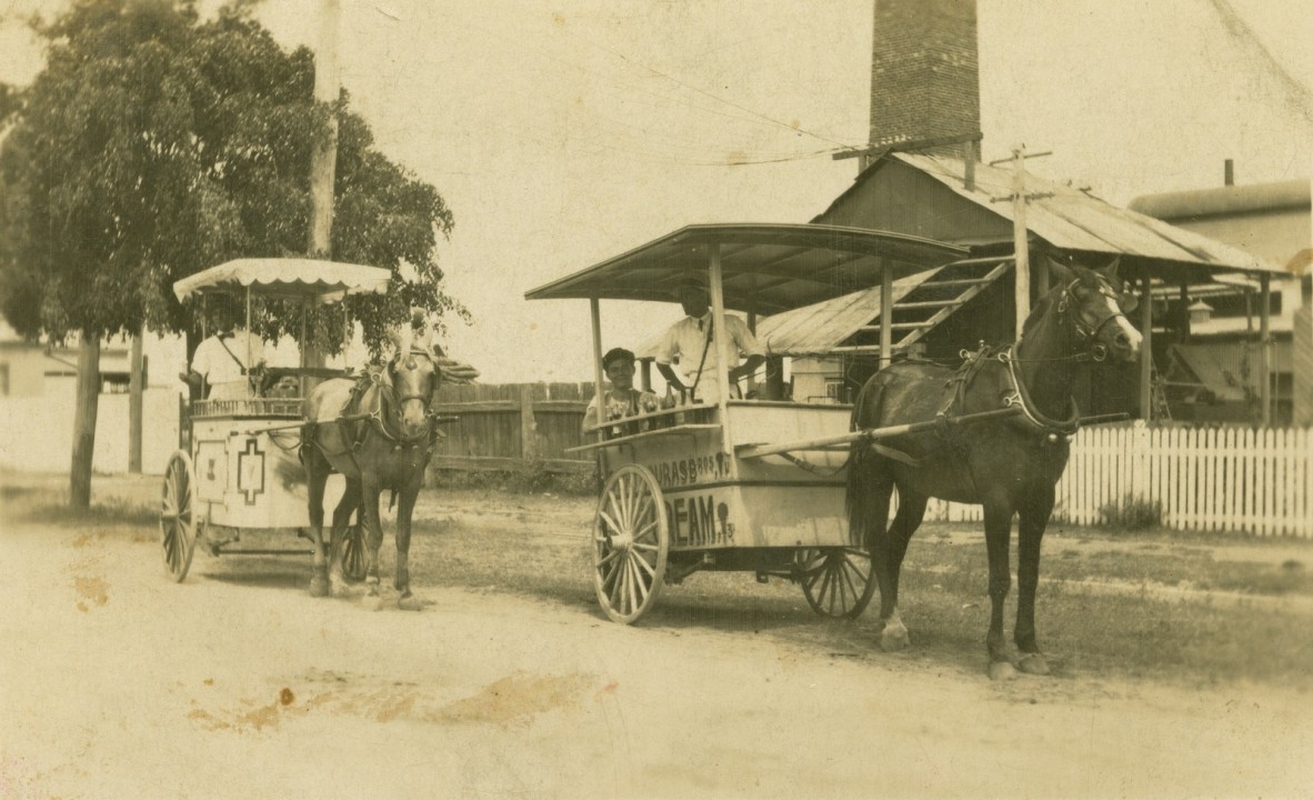 Two horse drawn ice cream carts carrying people down a dirt road