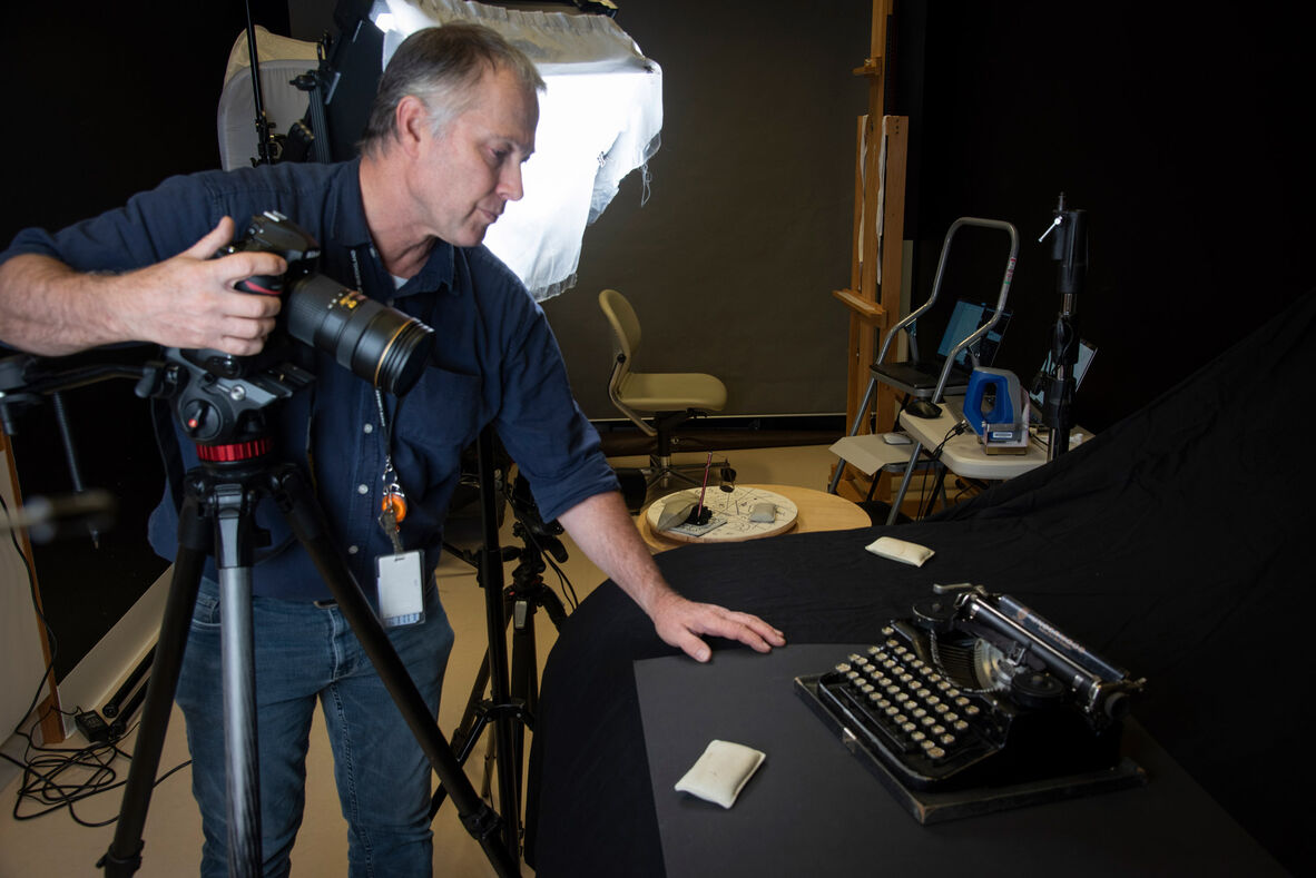 Photographer leaning beside camera to position antique typewriter he is photographing