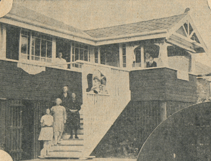 External view of Linga Longa, two story house with several people standing on the stairs leading up to the second level.