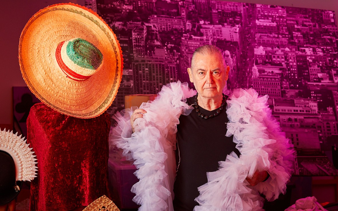 man wearing black shirt and pale pink ruffled robe with sombrero and artefacts on display