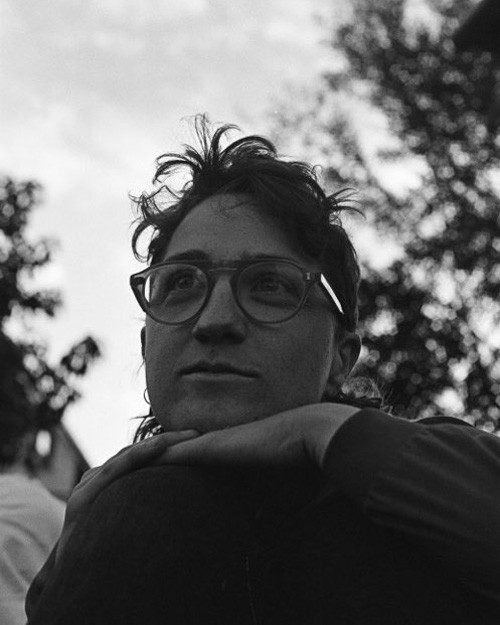 A black and white image of Marilena Hewitt They are wearing glasses and resting their face on their hands Theyre looking off camera