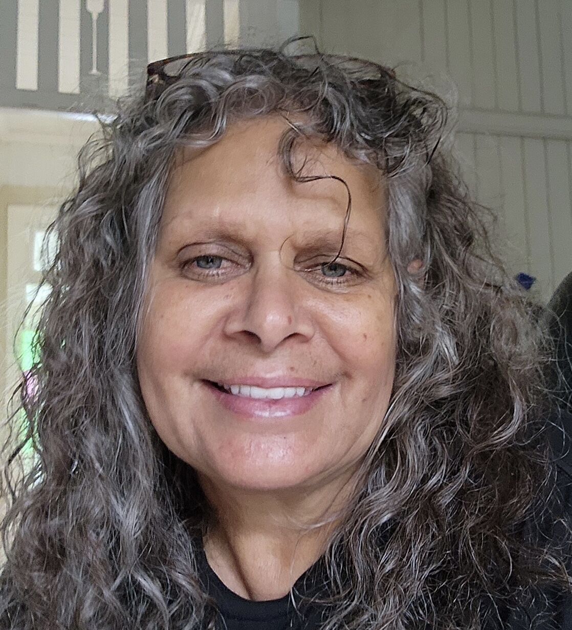 A smiling woman with brown skin and long curly grey hair.