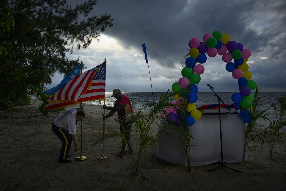A photo of a member of the US Services helping to secure the US and Solomon Island flags set up on Kennedy Island beach