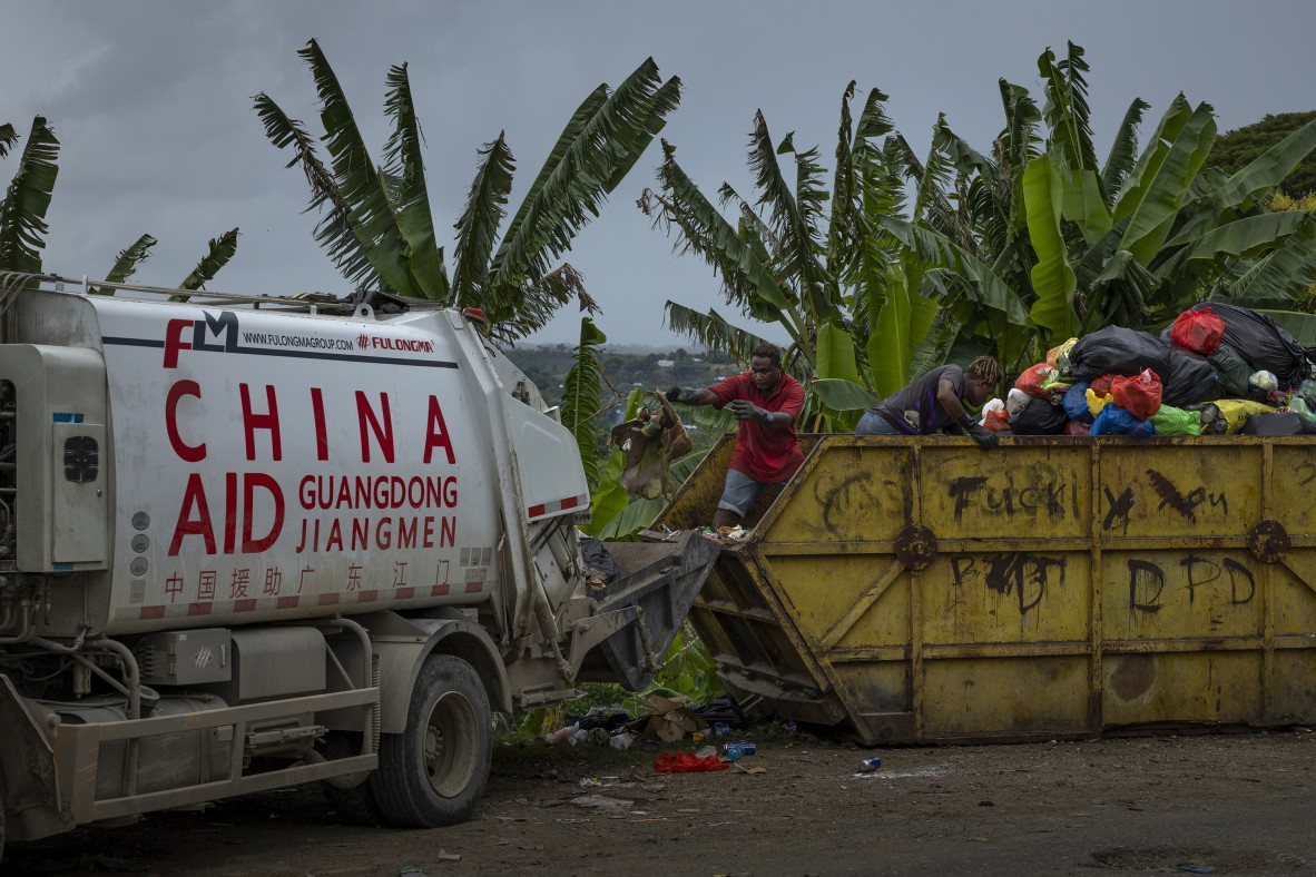 A photo of garbage collectors empty a large skip bin on the outskirts of Honiara