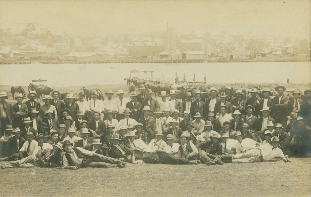 Large group of men sitting and standing with Brisbane River in background 1912