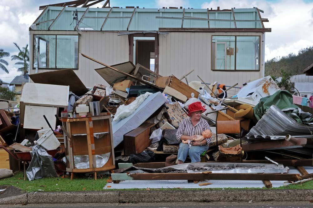 Minna Suchter surrounded by debris, cradles a doll rescued from a Tully home after Cyclone Yasi