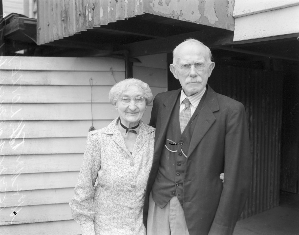  Couple wearing period clothing from an earlier time. Man wears waistcoat with watch-chain. Black and white photograph.