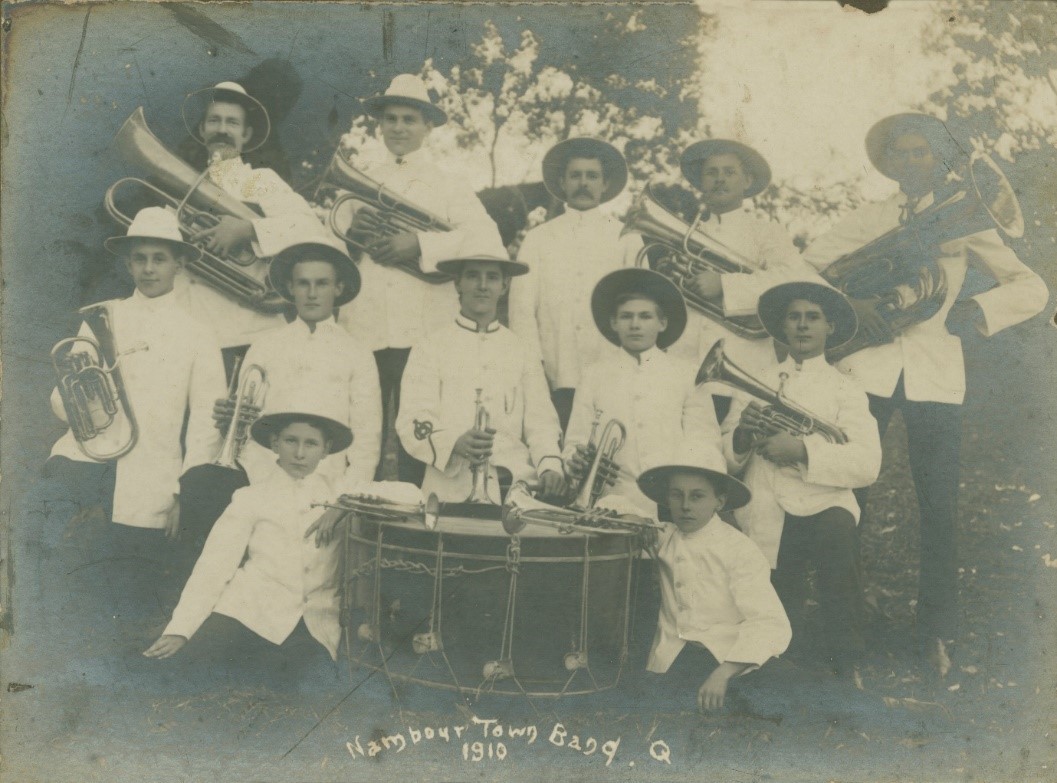 Sepia image of 12 brass band members kneeling and standing around a large drum Some are holding brass instruments