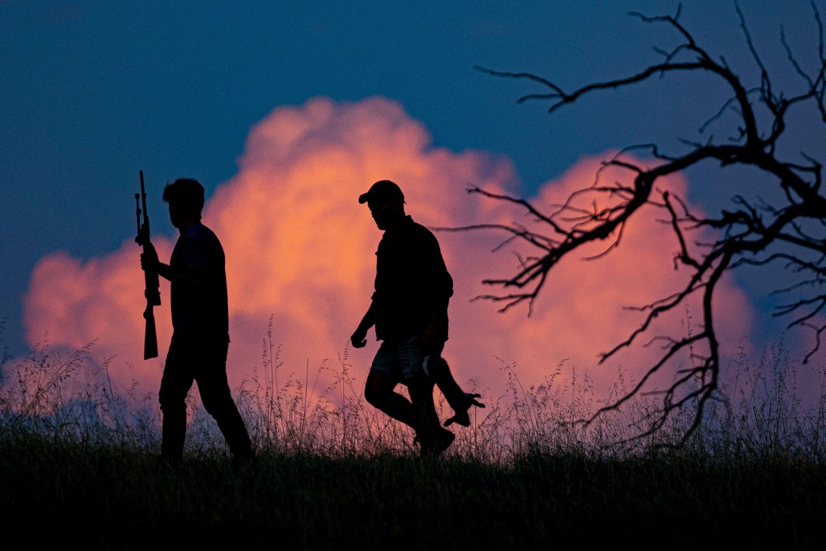 A photo of two men walking with guns and a dead rabbit silhouetted by a dark blue sky with pink clouds