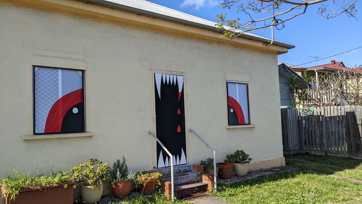 A small house is decorated to look like a monster’s face, with the door painted as a mouth with sharp teeth and the windows as big eyes, giving it a spooky, Halloween vibe.