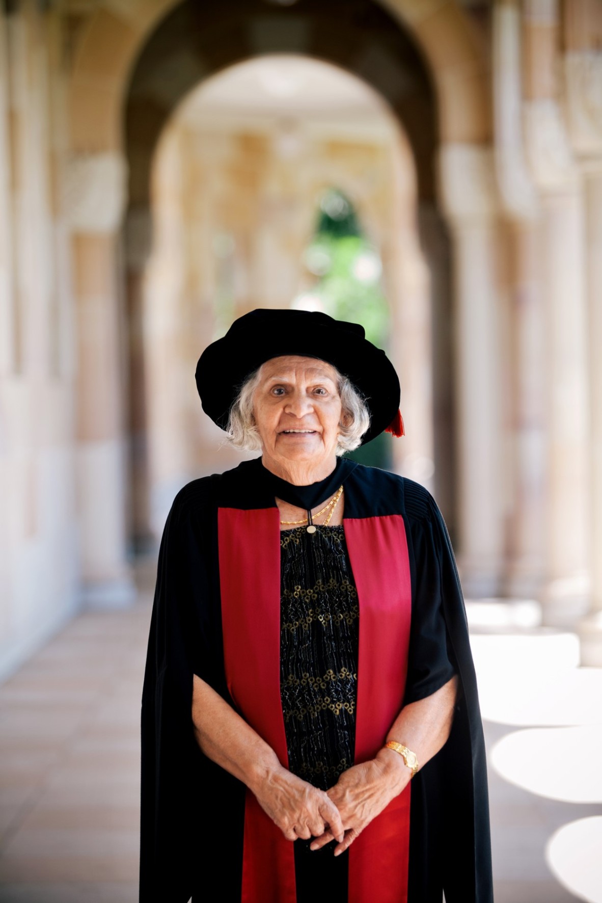 Older woman standing in stone hallway wearing graduation hat and gown.
