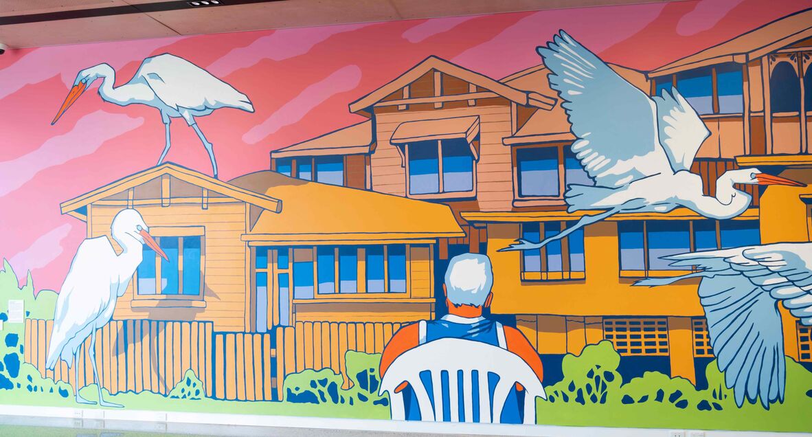 Mural of white-haired man sitting on plastic chair watching 4 egrets sit and fly around houses