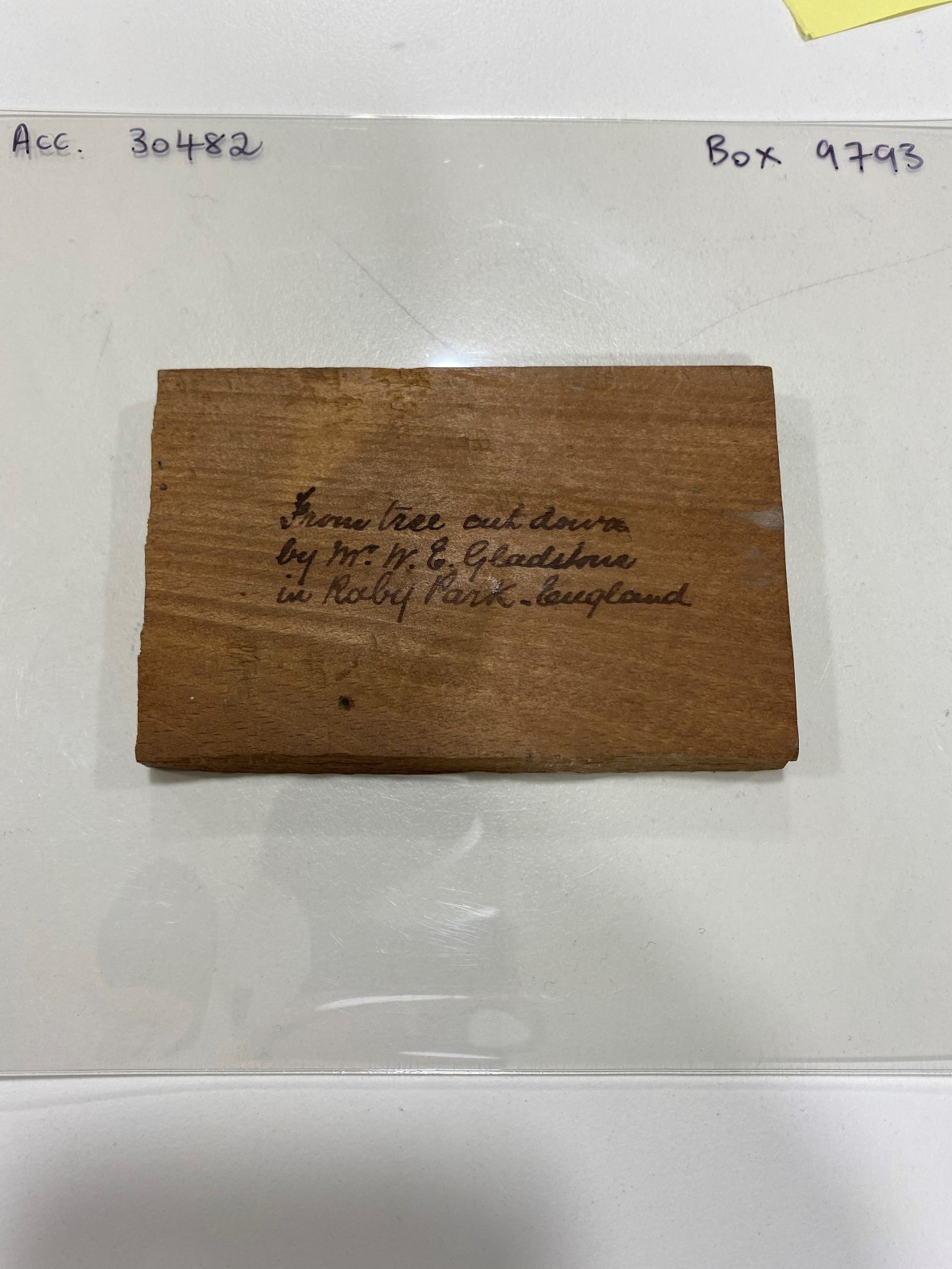 a rectangle piece of wood, with a short description written on it with a marker: "From tree cut down by M. W. E. Gladstone in Raby park, England."