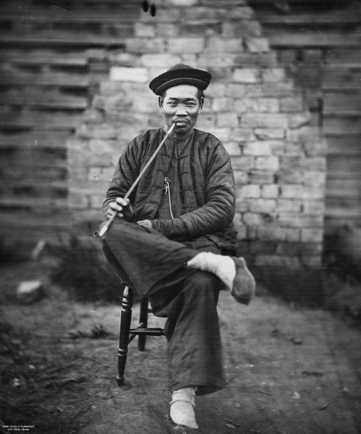Chinese miner in traditional garb relaxing with a long stemmed pipe