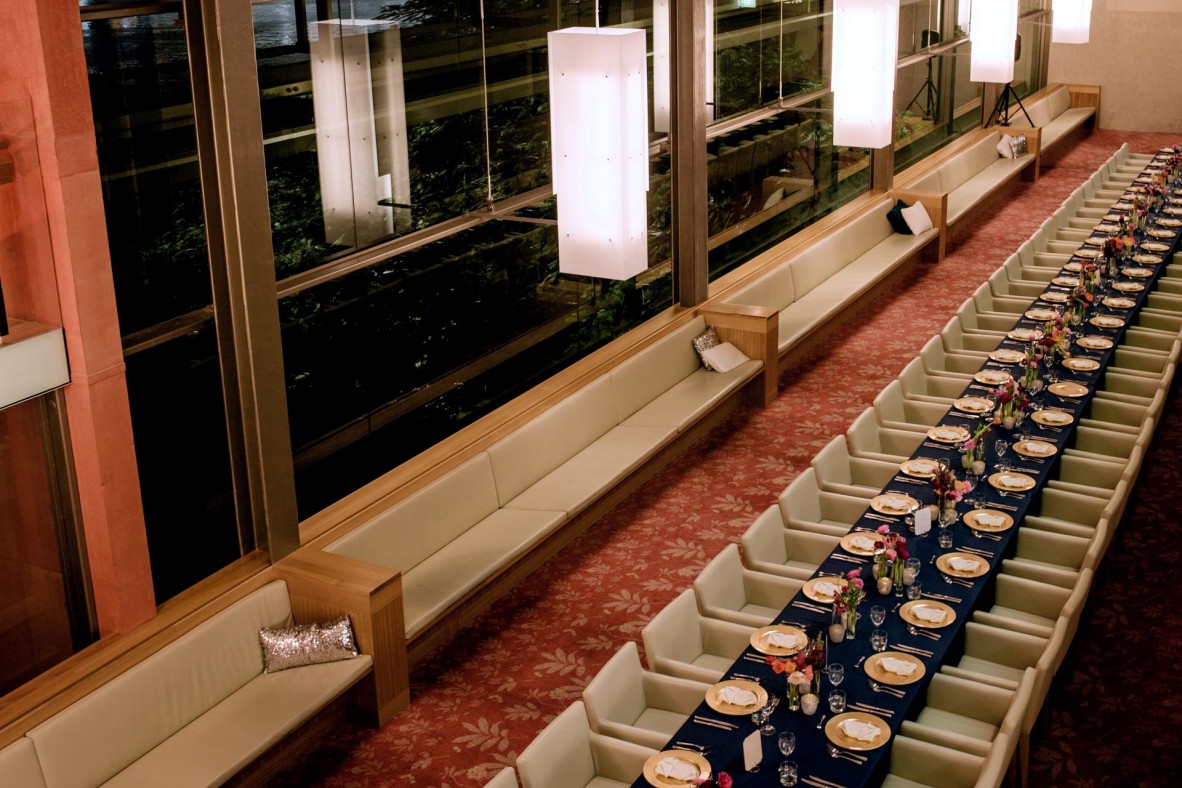A long dining table set with dinnerware and surrounded by chairs in the Poinciana Lounge at State Library.