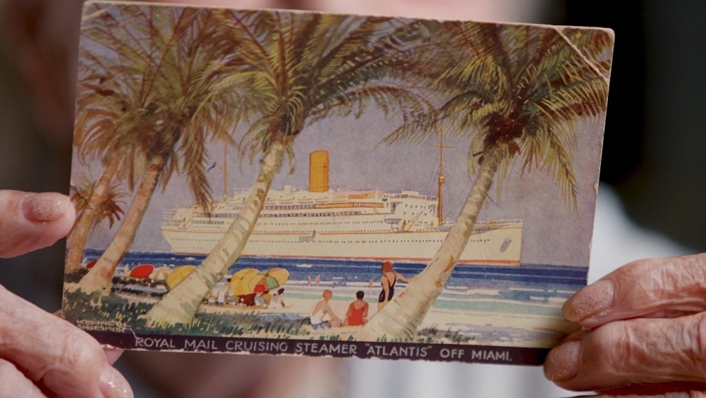 Jackie McLaughlin holding a postcard of the ship Atlantis, the ship that took her to her new life in Queensland as a War Bride.