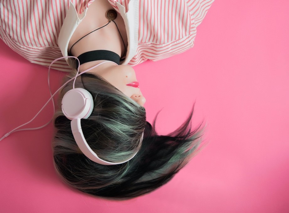 A girl laying down listening to pink headphones