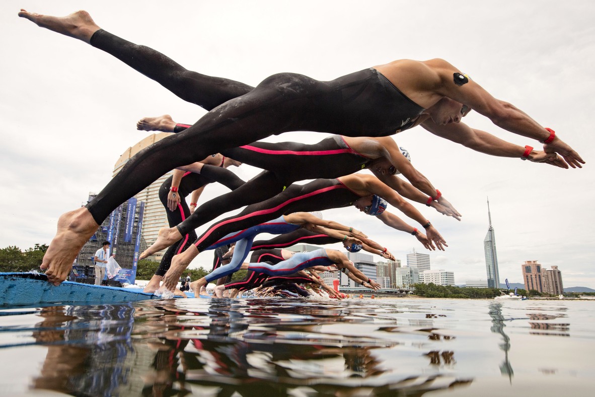 A photo of a group of divers launching into a pool for a competitive race