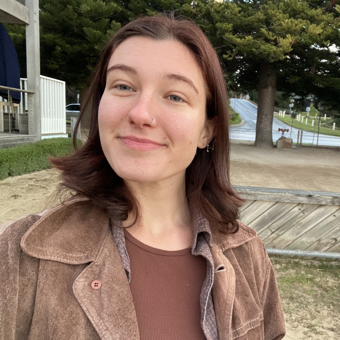 A selfie of Quinn Stennett who has short brown hair and is standing, smiling, in a park