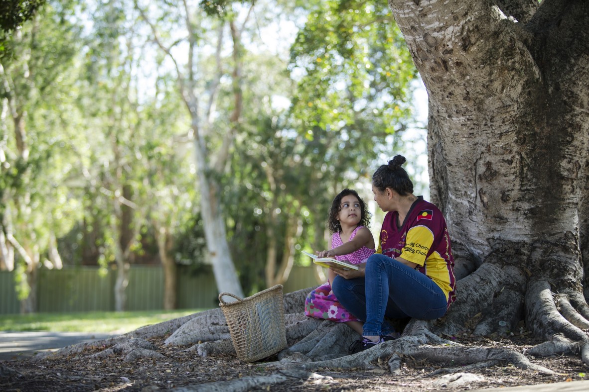 Mother and daughter reading a book under a tree