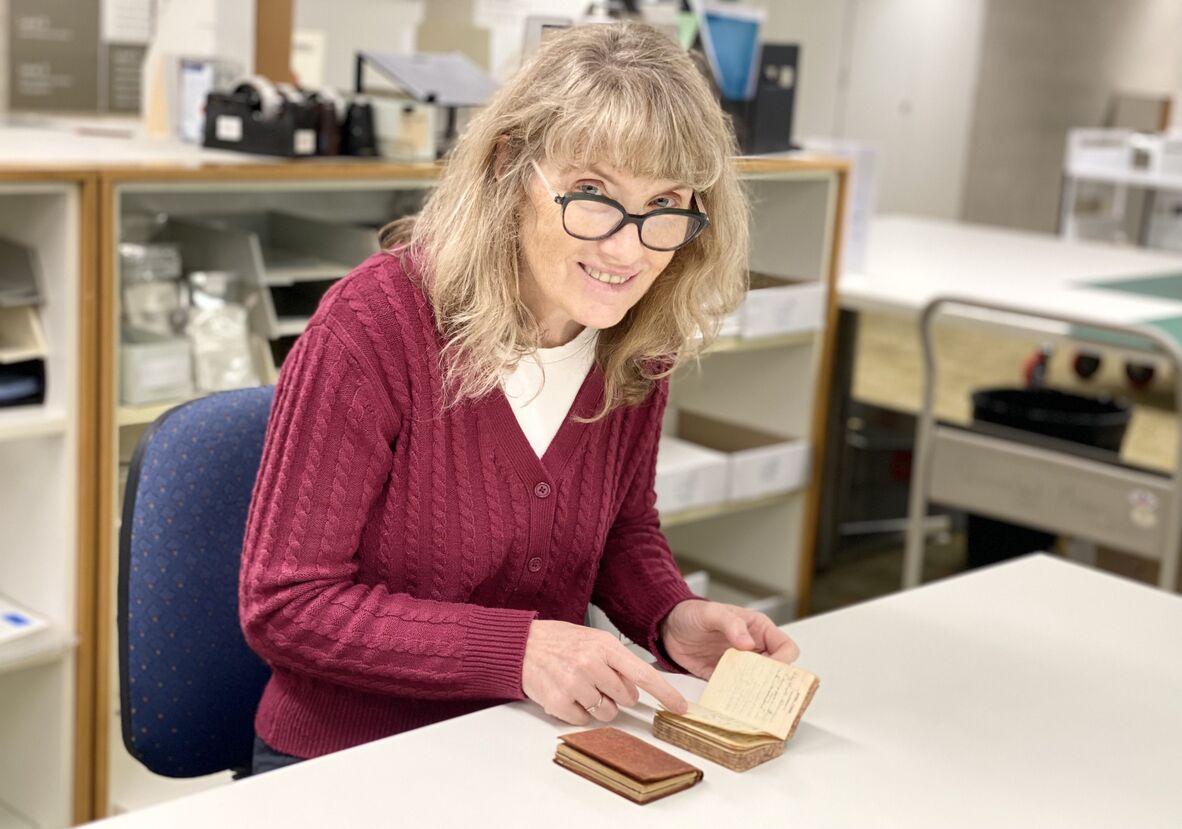 Woman with long blonde hair and glasses in red cardigan reading old diaries