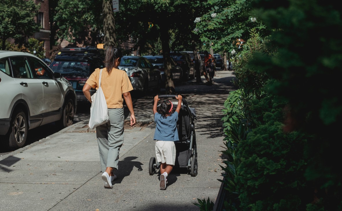 Mother and preschooler walking down the street, preschooler is pushing a pram