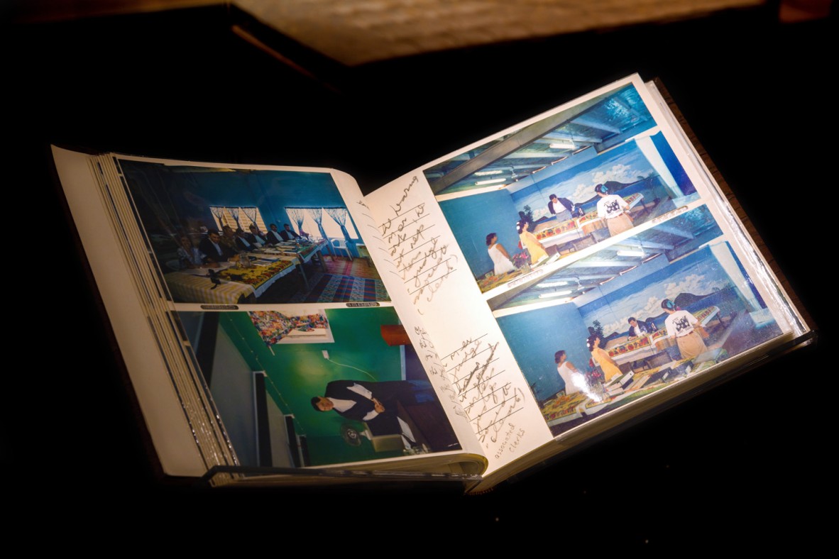 Open photo album on a stand behind a glass cabinet.