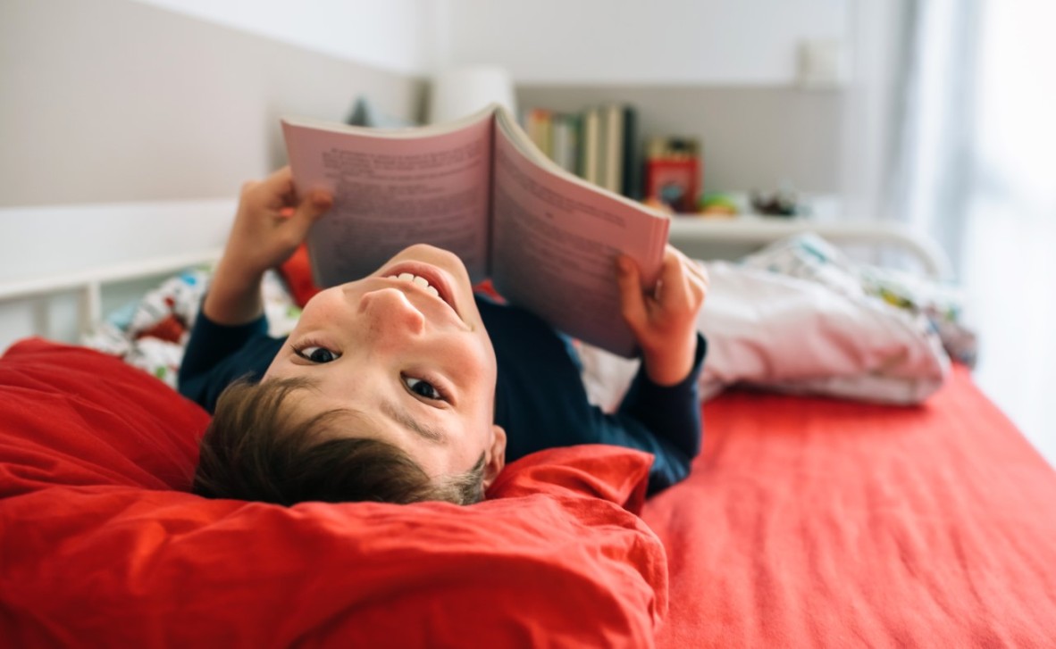 Boy lying in bed reading looking backwards