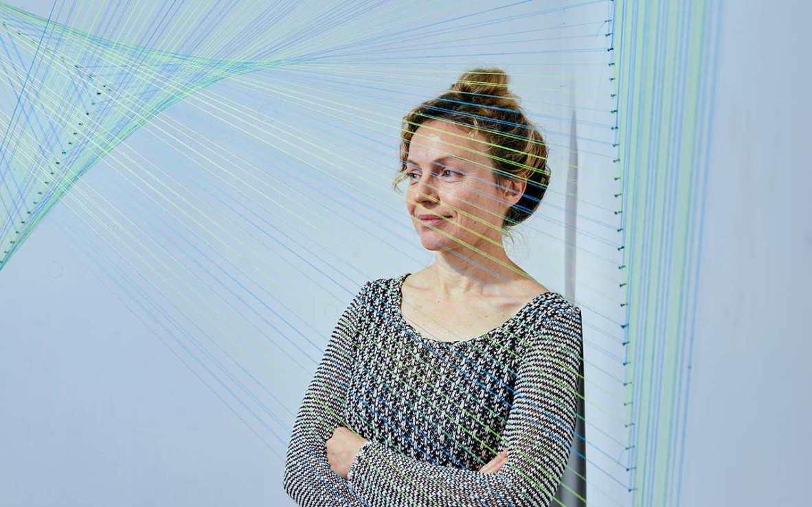 woman standing behind intricate thread installation artwork