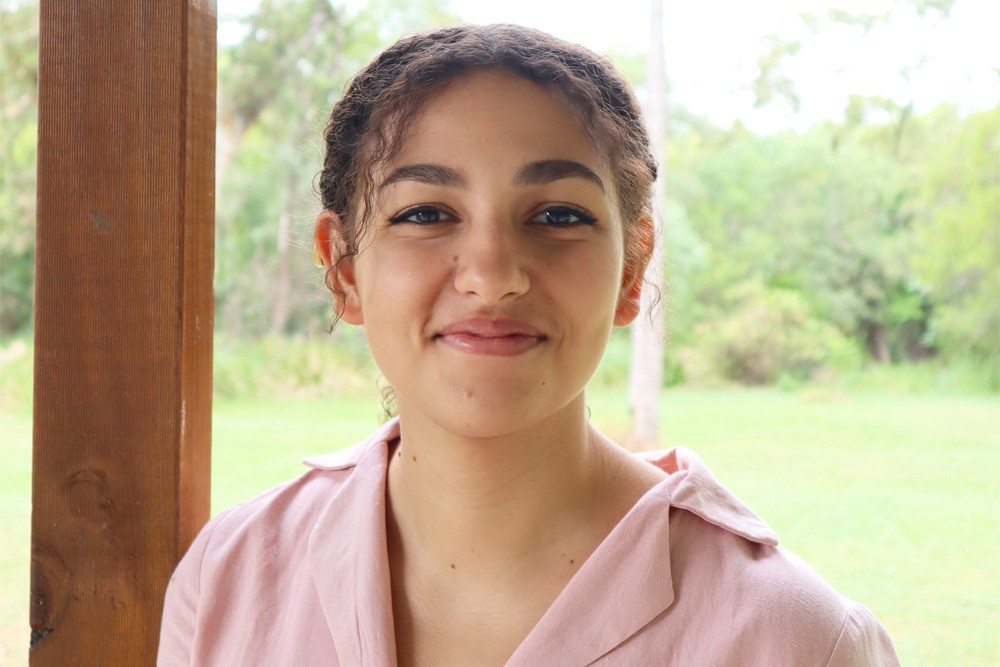 A young woman in a pink button down shirt, with green lawn behind her