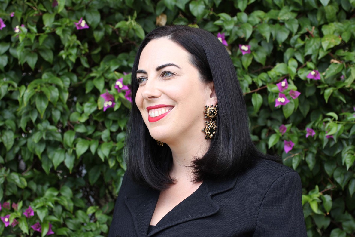 Smiling, dark-haired woman wearing black suit and statement earrings