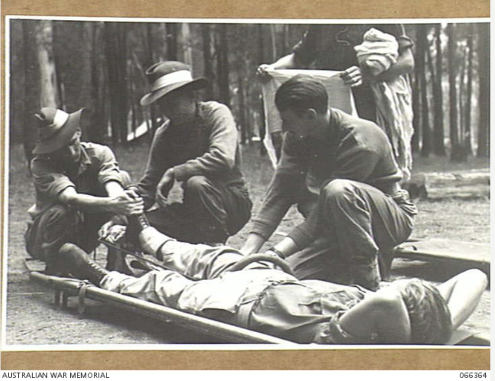 Four soldiers attending to a soldier lying on a stretcher with his right leg in a splint