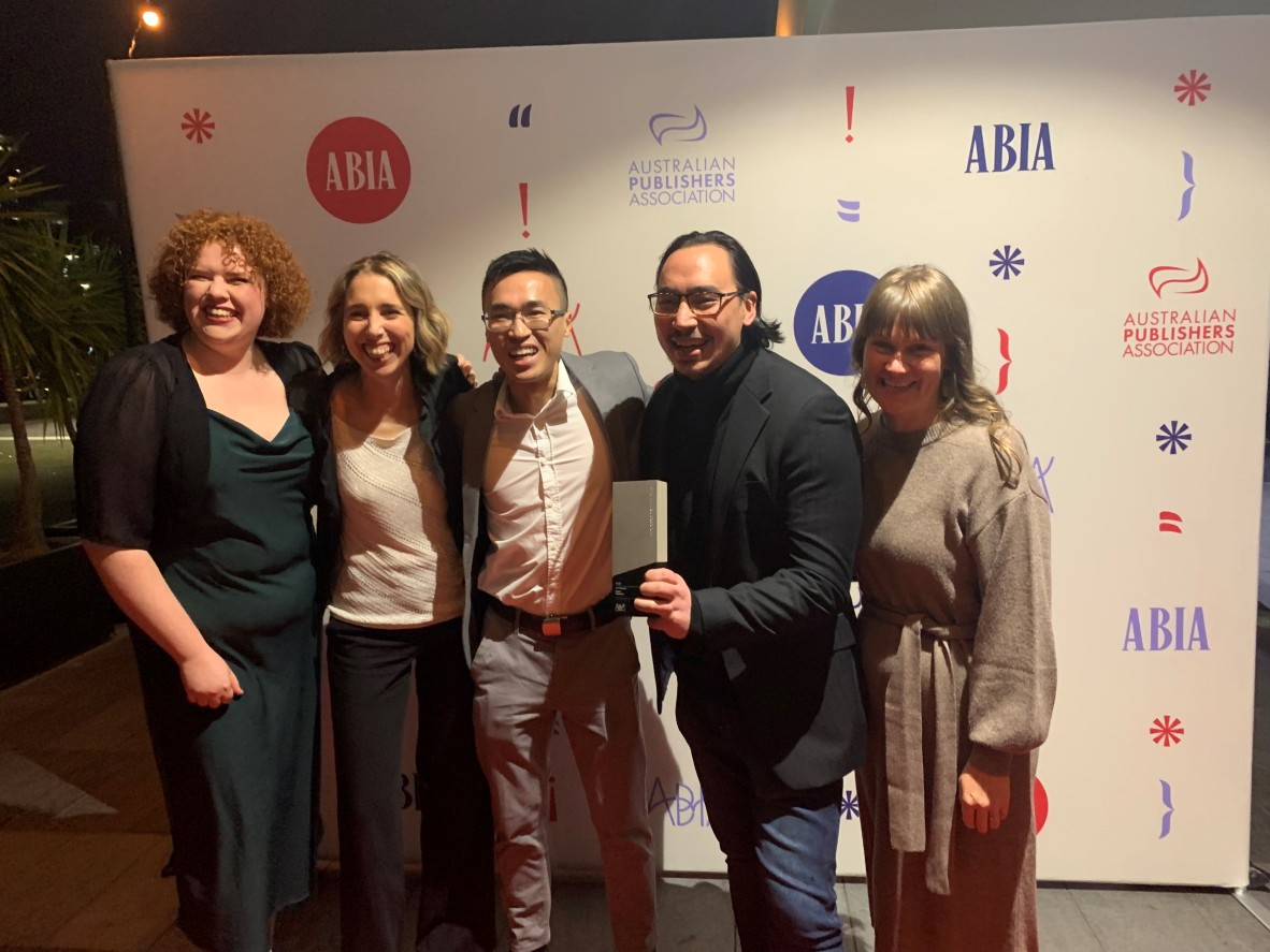 Five people stand smiling at an awards show; one of them holds a trophy