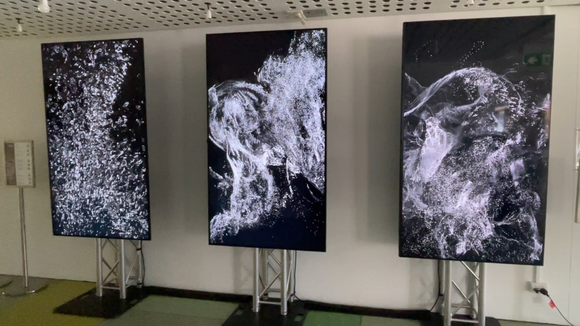 A photo of three vertical screens with black and white point cloud artwork