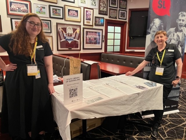 Two State Library staff members standing by the exhibitor stall for State Library at the Sands of Time Conference 2022