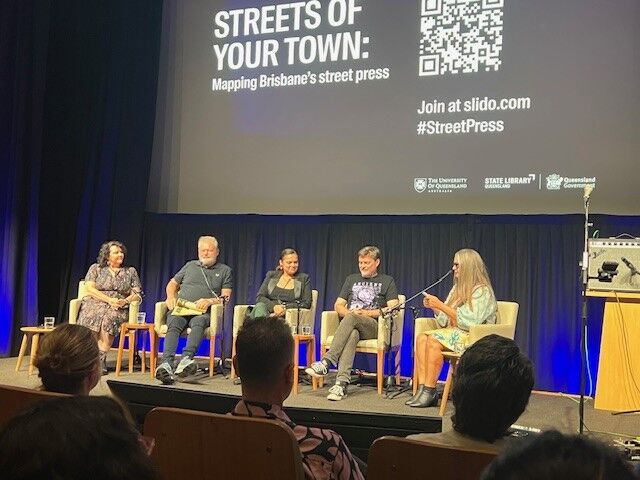 A panel of 5 speakers sits onstage in an auditorium. Above them the screen says Streets of your town: Mapping Brisbane's street press.