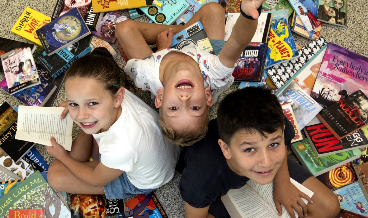 A girl and two boys surrounded by a pile of books