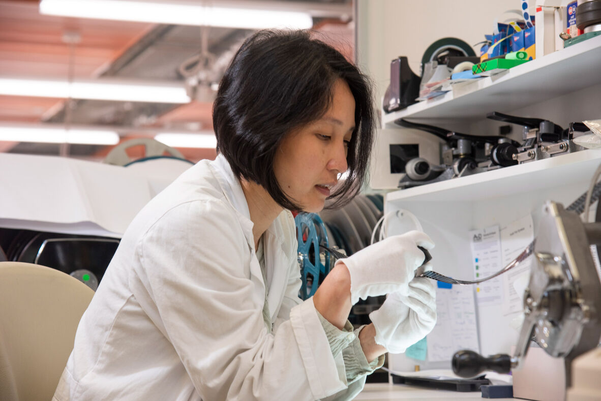 Woman in lab coat examining section of film with magnifier