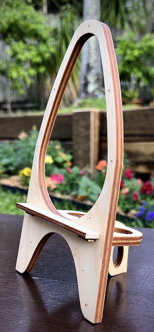 a photo of a round wooden laser cut mini easel sitting in the foreground of a grassy background.