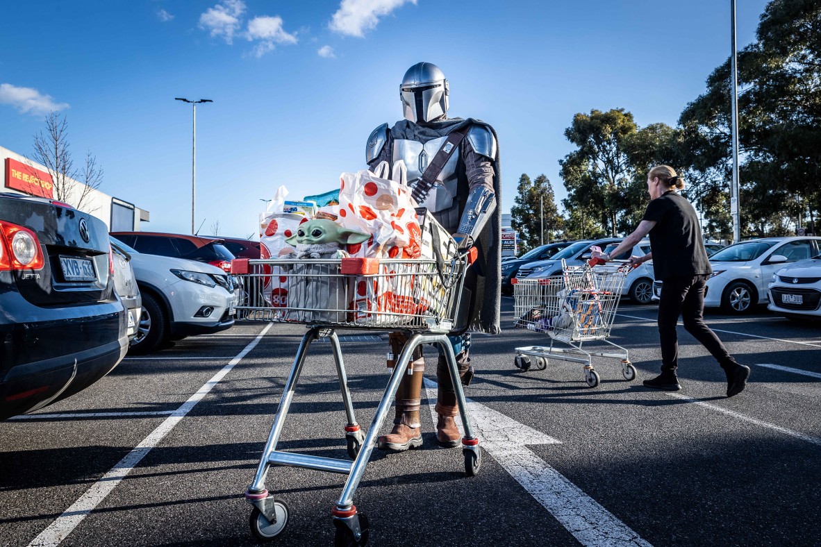 A photo of someone in a Mandalorian costume pushing a trolley with Grogu in it