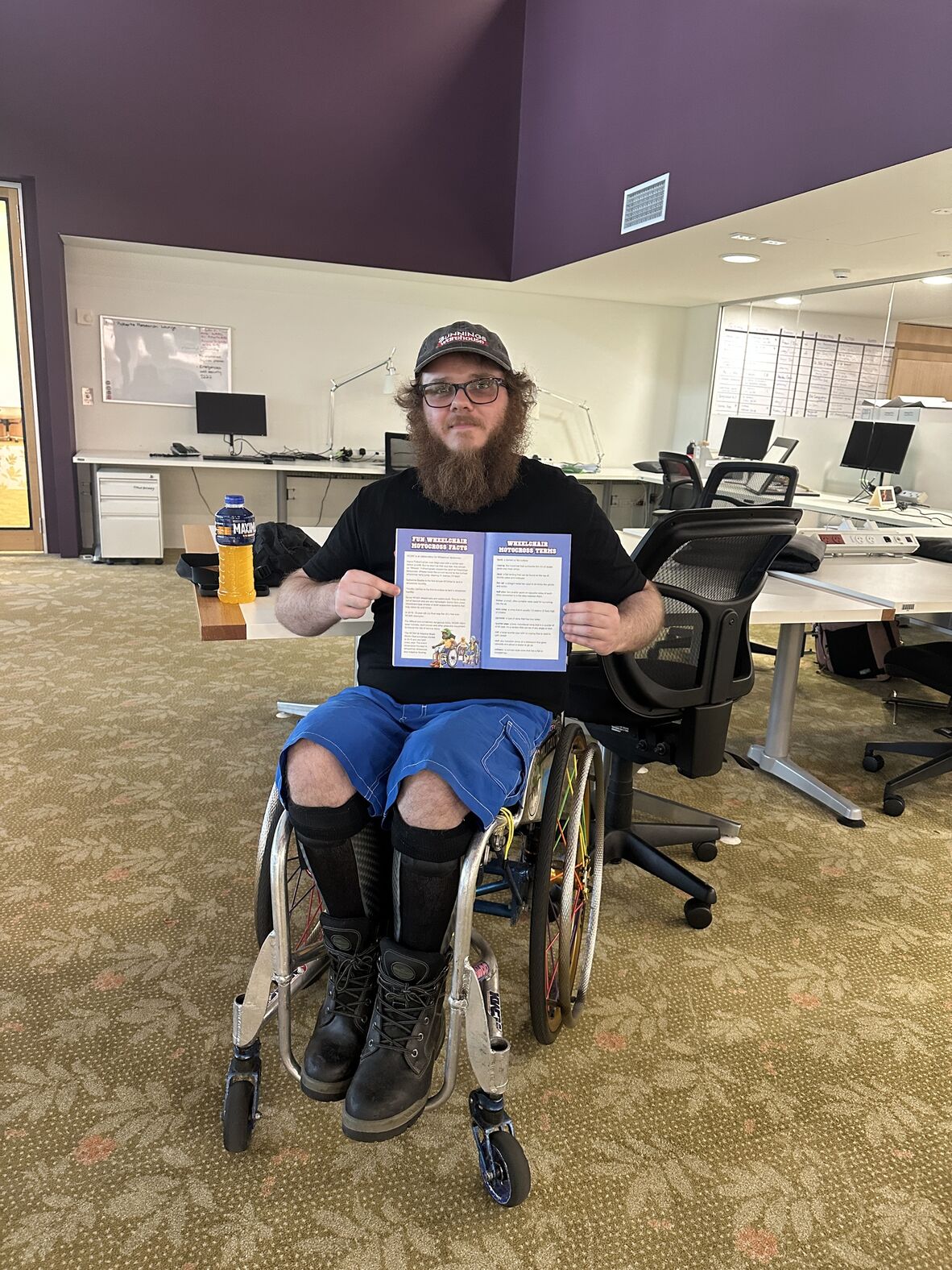 Timothy Lachlan, seated in a wheelchair, poses for the camera while holding up a graphic novel