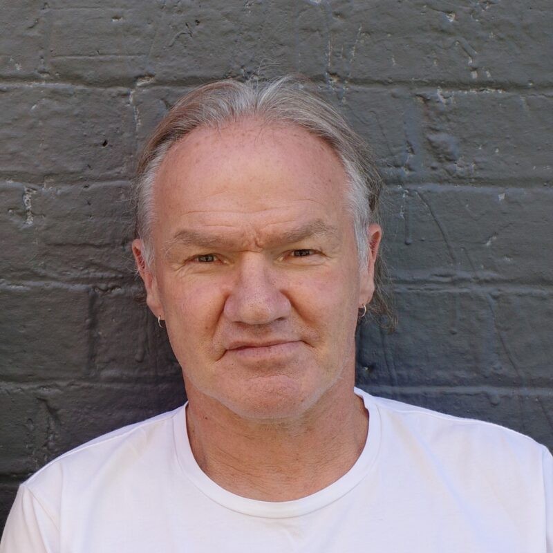 A picture of a man in a white shirt with a brick wall in the background