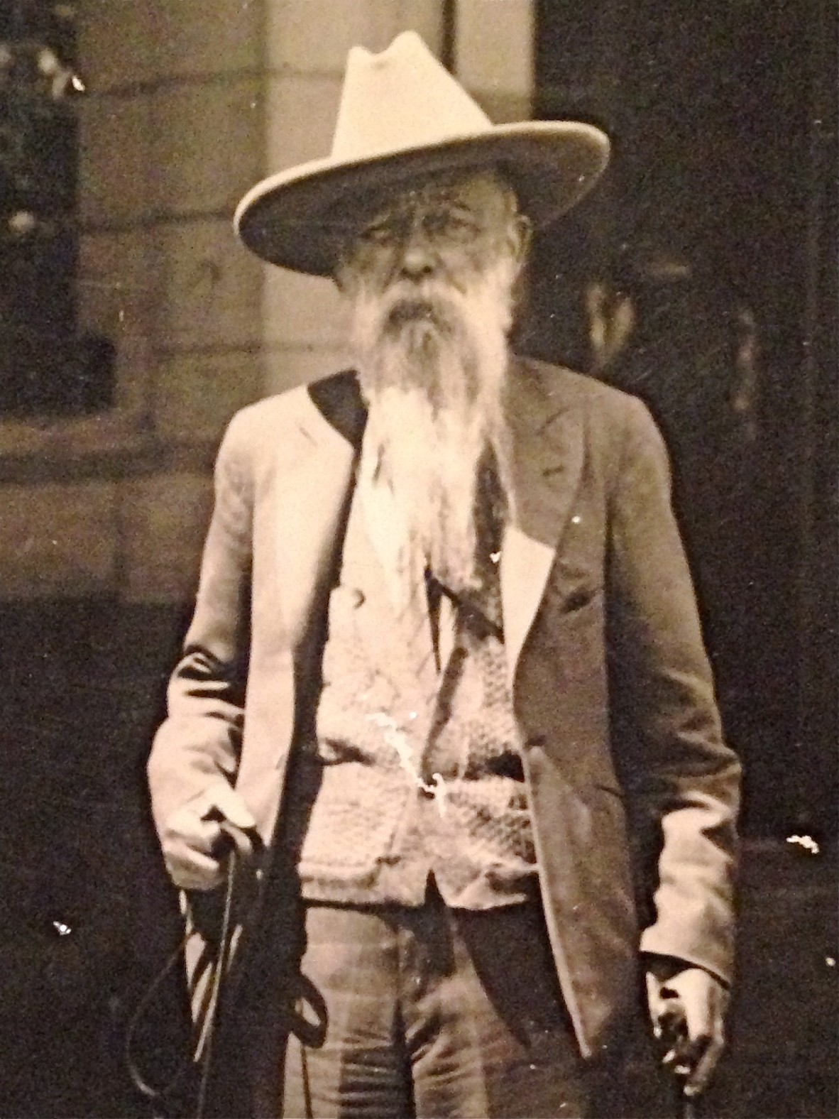 Sepia image of man with a long beard wearing a jacket and vest, holding a leash in right hand