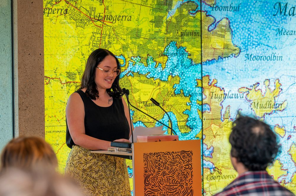 Young woman with dark hair and glasses standing at podium in front of map background