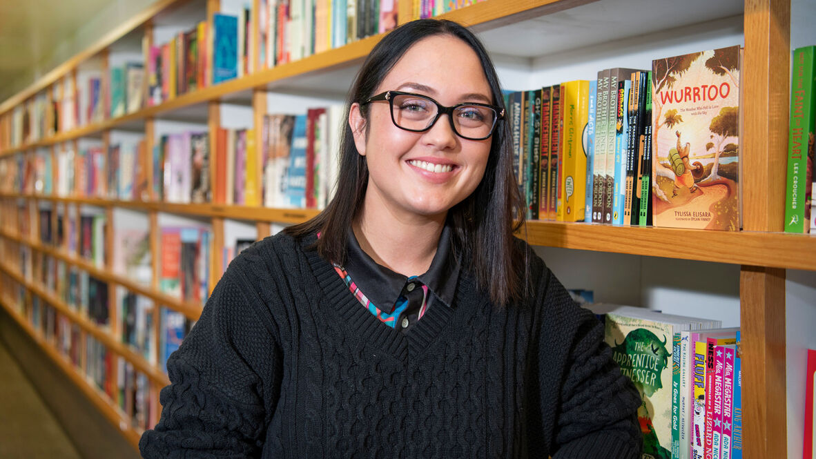 Young woman with dark hair and glasses standing next to bookshelf