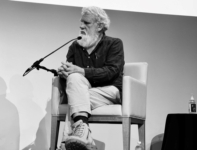 A black and white image of Uncle Bruce Pascoe sitting down and speaking at Brisbane Writers Festival in 2021.