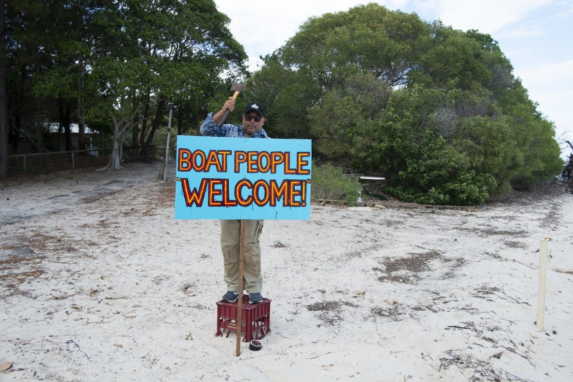 Gordon Hookey placing a sign reading 'Boat people welcome' in the sand in preparation for the arrival of industry representatives by boat, Gold Coast Indigenous Artist Camp, South Stradbroke Island, May 2019