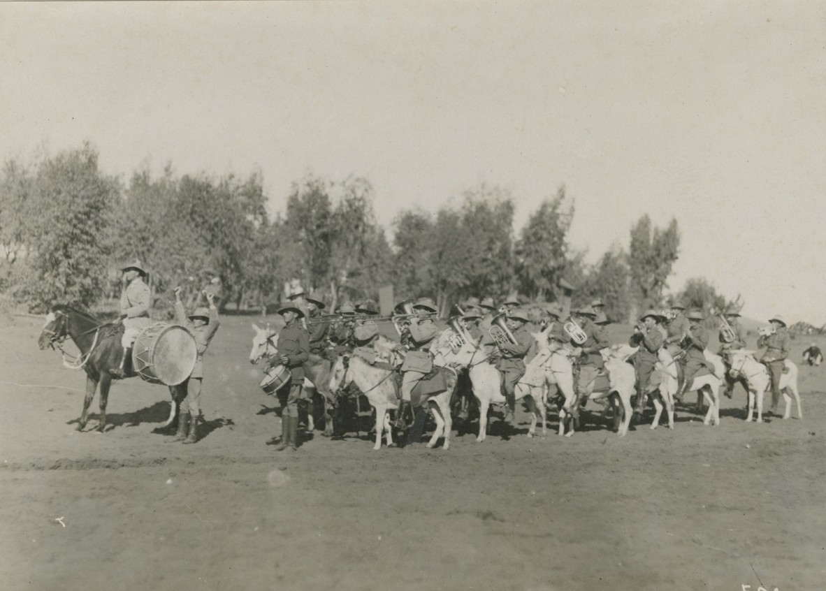 Group of approximately 20 soldiers in uniform facing left of camera point of view riding donkeys Soldiers playing brass instruments and drums 