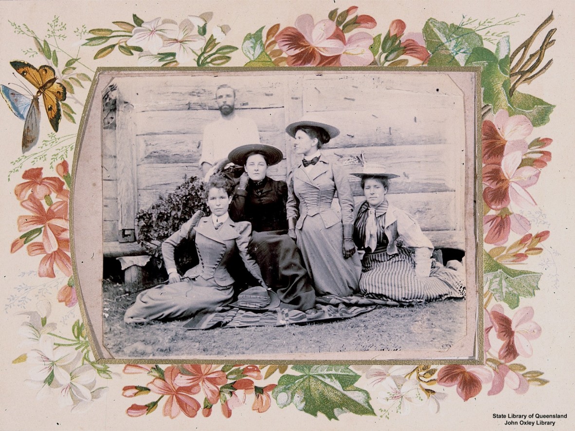 A group of four women and one man sitting outside a wooden house