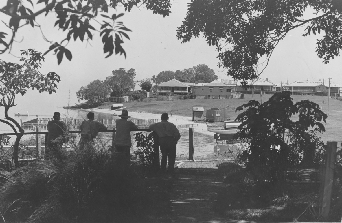 Four men leaning on a fence overlooking the benevolent asylum at Dunwich, Queensland, 1938